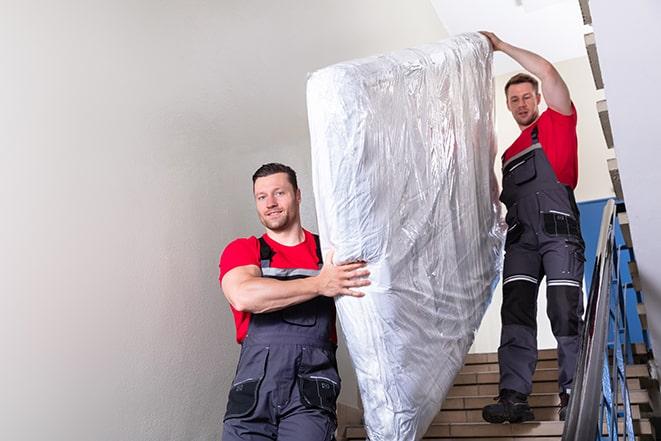 man carrying a heavy box spring out of a room in Clayton